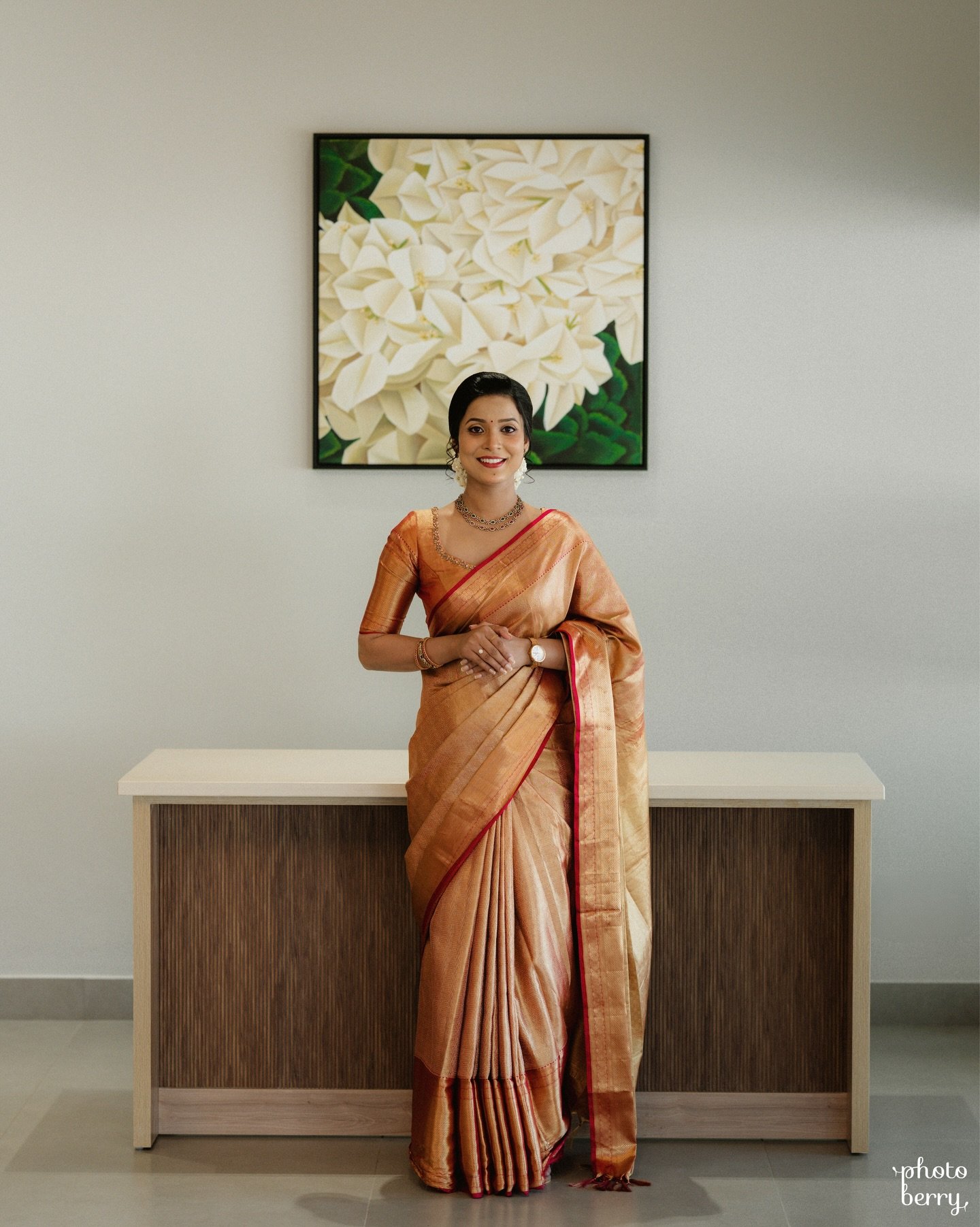 A bride in a copper saree standing beneath floral artwork